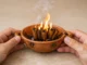 ritual canela prosperidad abundancia — ramas de canela ardiendo en cuenco de barro con manos sosteniendo