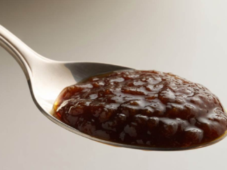 Primer plano nítido de una cucharada colmada de una mermelada espesa, de color marrón oscuro, hecha con ciruelas pasas y dátiles. La imagen representa el laxante natural casero para combatir el estreñimiento y promover la limpieza del colon.