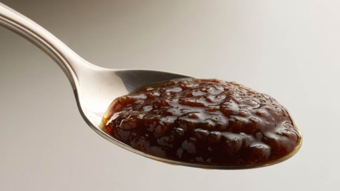 Primer plano nítido de una cucharada colmada de una mermelada espesa, de color marrón oscuro, hecha con ciruelas pasas y dátiles. La imagen representa el laxante natural casero para combatir el estreñimiento y promover la limpieza del colon.