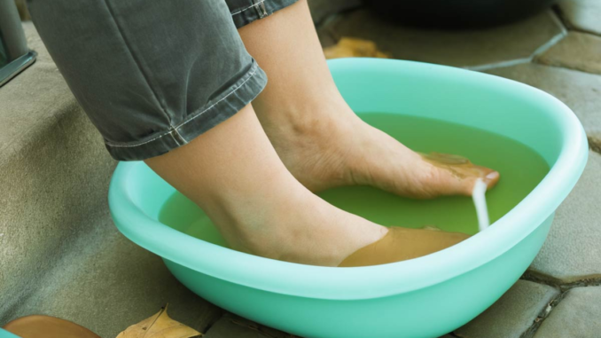 Pies de una persona sumergidos en un recipiente con agua y vinagre (pediluvio), remedio casero para eliminar hongos y el mal olor.