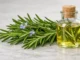 Ramas frescas de romero con flores junto a un frasco de aceite esencial de romero sobre una superficie de mármol