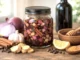 Frasco con jarabe de cebolla morada, ajo, canela y especias macerando en vino tinto, junto a los ingredientes de la receta