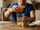 Mujer rompiendo un huevo en un vaso con agua sobre una mesa de madera, ritual tradicional de limpia energética