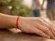 Hilo rojo atado en la muñeca de una persona, con una pareja tomada de la mano desenfocada de fondo